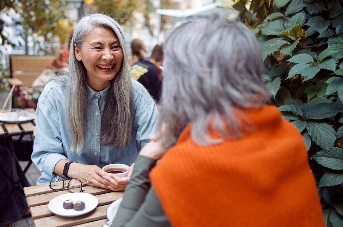 laughing-mature-asian-woman-with-friend-at-a-table-on-an-outdoor-terrace